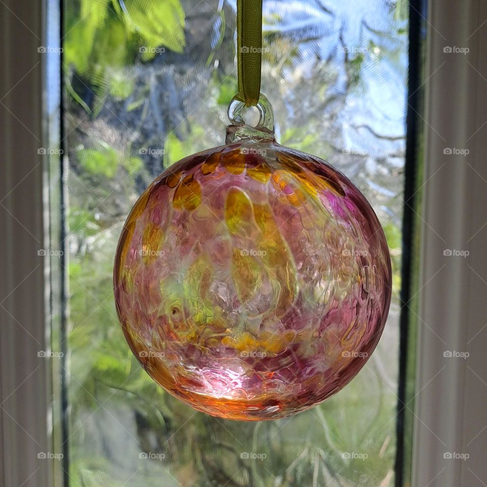 glass ball hanging in front of glass window with daylight and green fiage outside