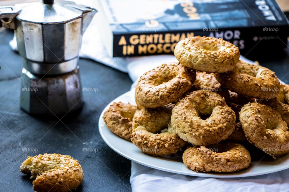 Traditional Maltese biscuit known as Qaghaq tal-Gunglien. Placed on a white plate with a small coffee pot at the side and a book in the background.