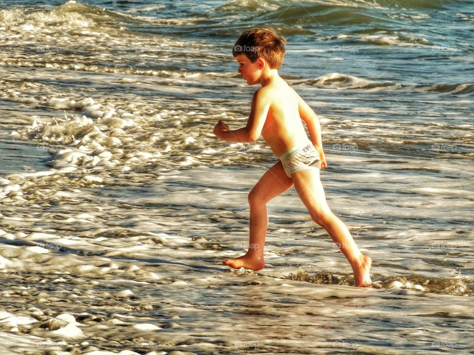 Young Runner. Boy Running From Ocean Waves