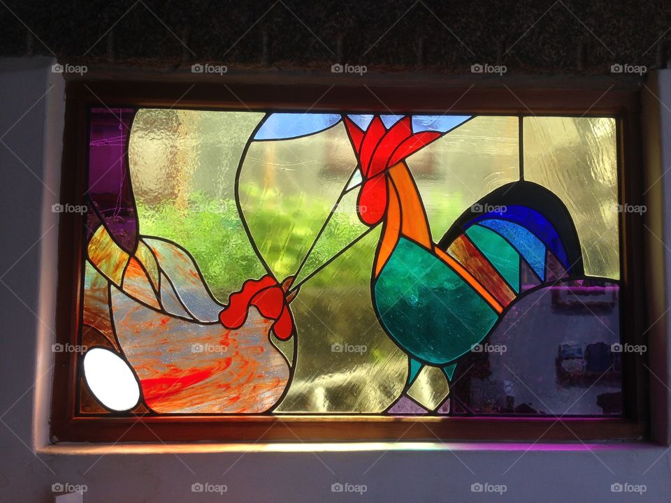 A modern stain glass window in Cornwall, depicting a rooster and a submissive chicken with her egg.