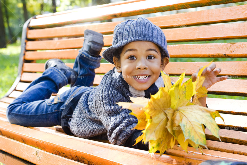 Boy lying on wooden bench and holding autumn leaf