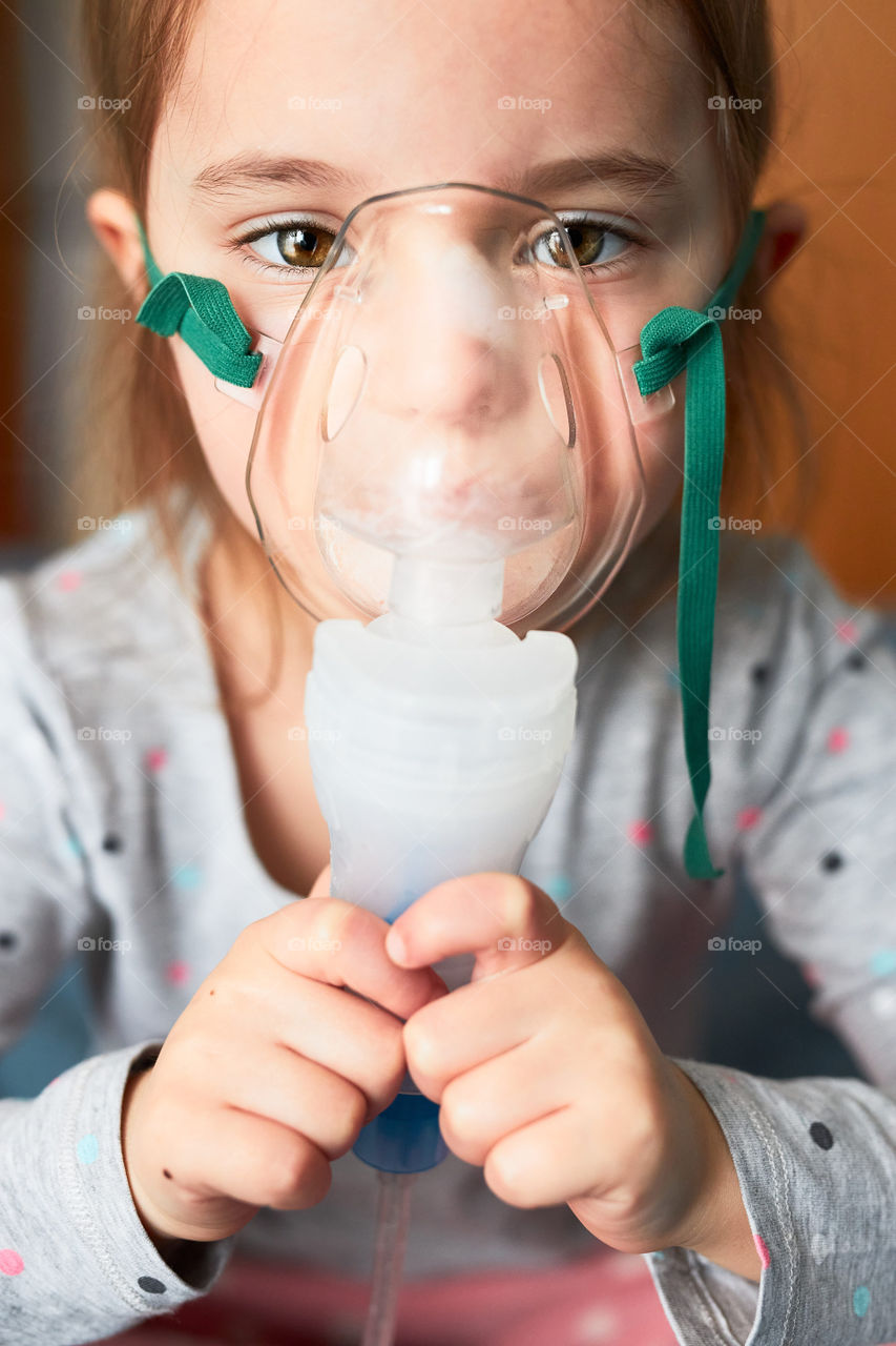 Sick little girl having medical inhalation treatment with nebuliser. Child with breathing mask on her face lying in bed