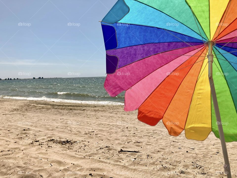 A sunny day at the beach under a rainbow umbrella.