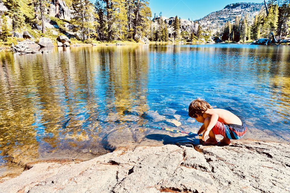 After a long day hike from the car to camp lake, the boy was touching the cold water of the lake. 