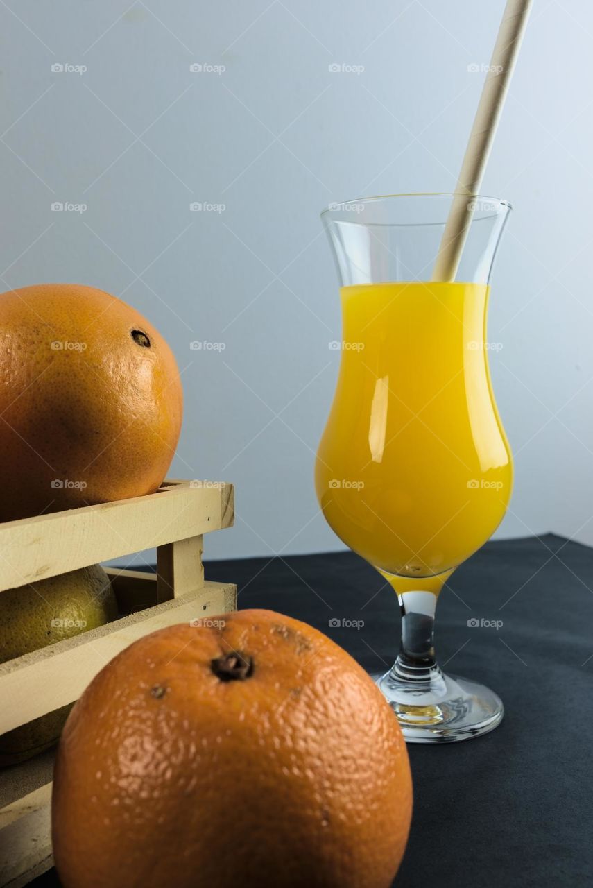 Oranges and glass tumbler with orange juice on black background