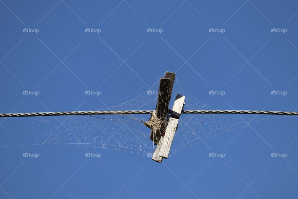 Two old and weathered clothes pegs with spiderwebs clothespins on clothesline against a vivid blue sky, 