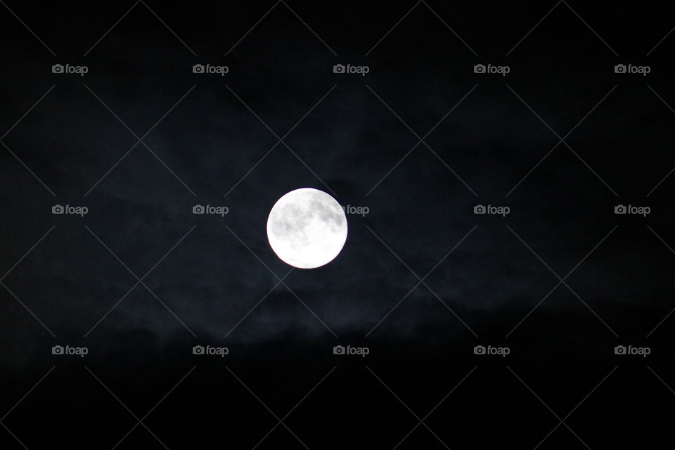 A bright full moon in a cloudy night time sky