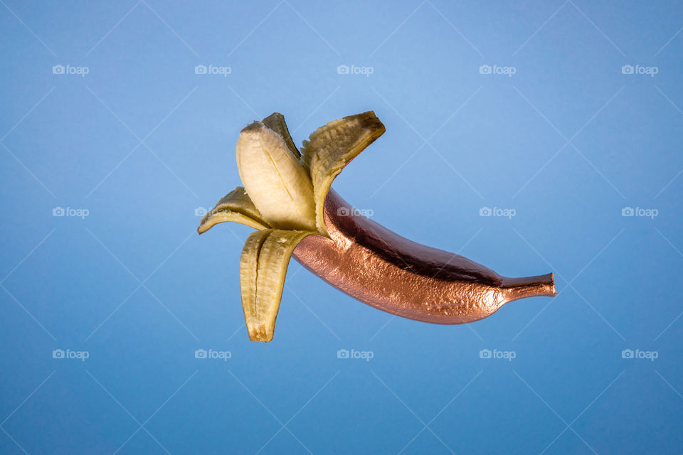 Floating gold banana on blue background. Minimal food concept