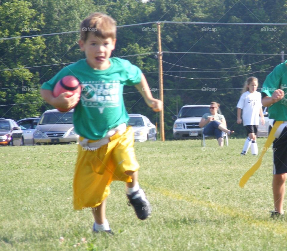 Young boy running with football during flag football game