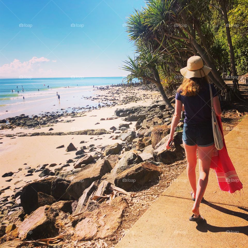 Walking along the beach with blue sky blue sea and warm yellow sand, girl with hat