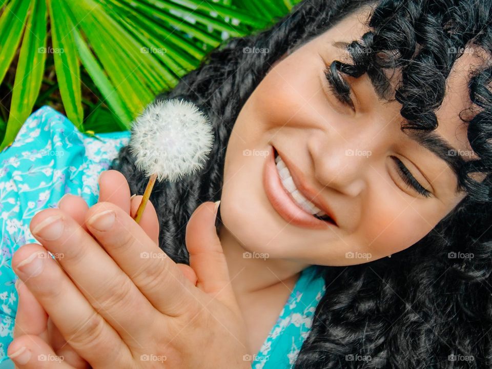 Woman smiling and looking at a dandelion before blowing it away.