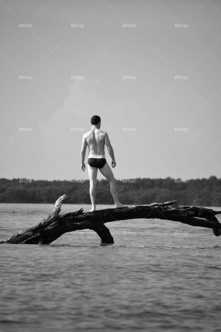 Rear view of a shirtless man standing on tree trunk