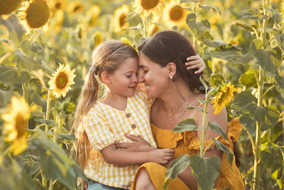 Lovely mother and daughter hugging in beautiful sunflower field on sunny summer day