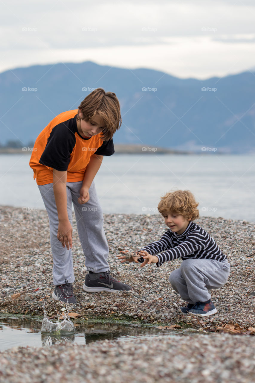 two boys brothers playing with stones at the beach