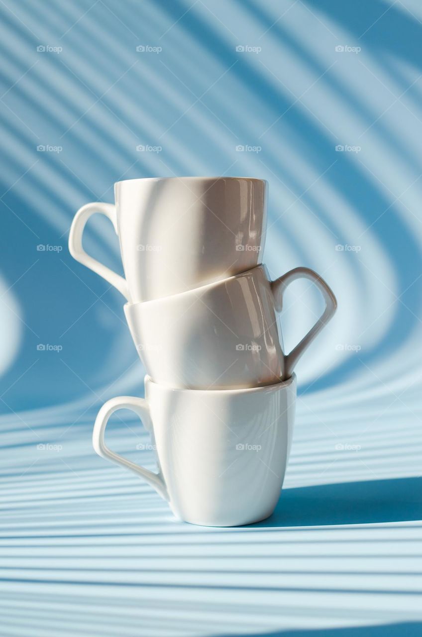 Three white cups of hot black coffee,  tea against blue background close up. Breakfast time.