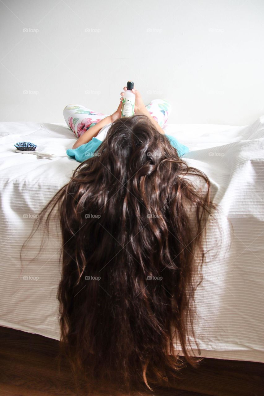 Child with long healthy hair is laying on a bed