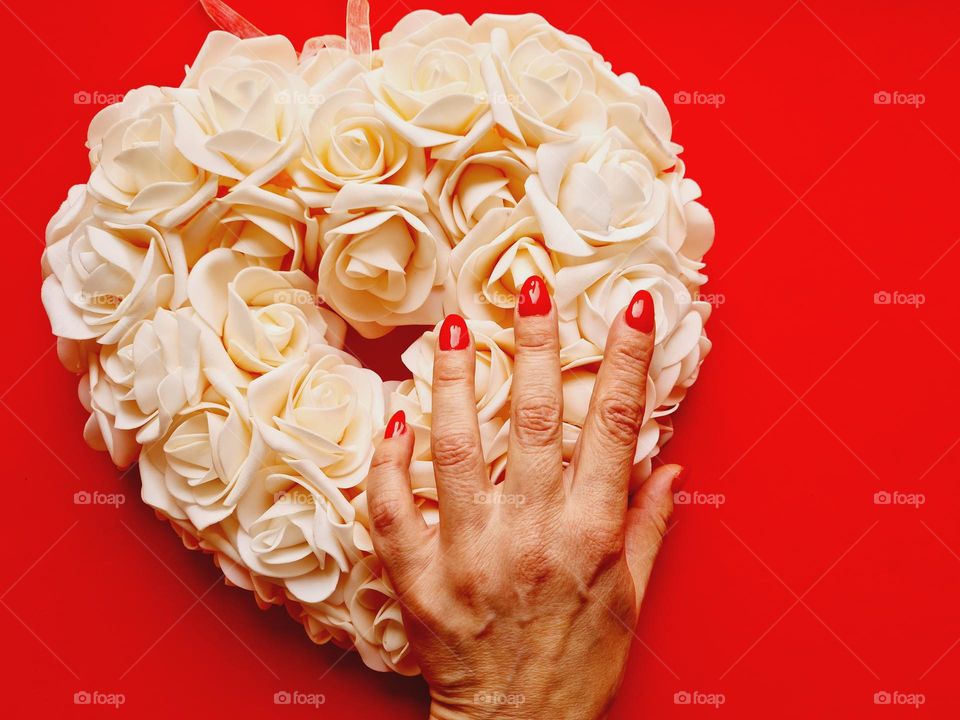 hand with red painted nails on a pillow of heart-shaped roses