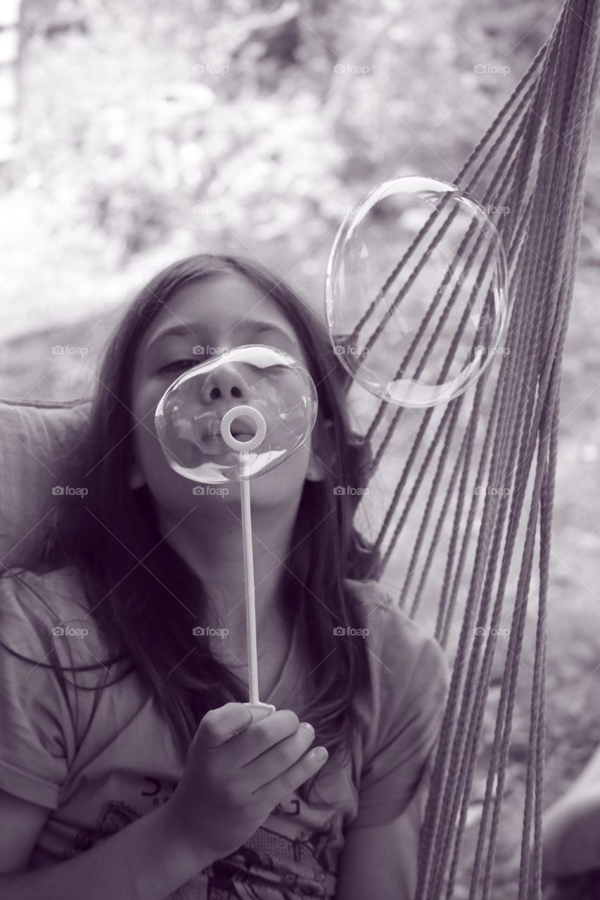 Kid sitting on an hammock and blowing soap bubbles 