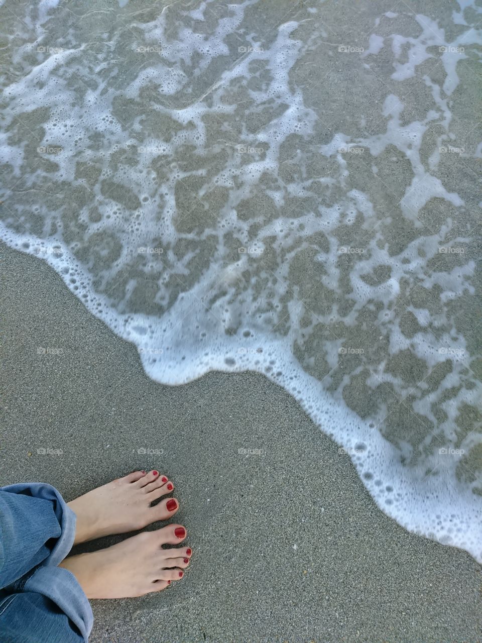 Feet with Red toe nails on sand beach with white froth wave