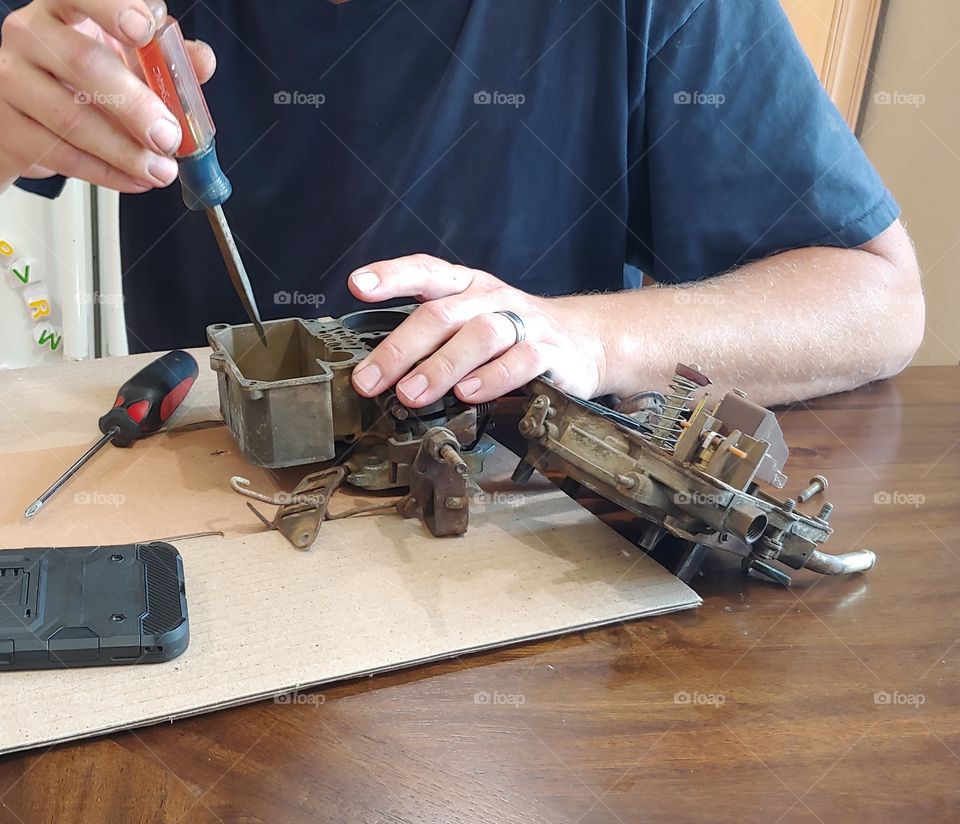 Automotive Carburetor Repair - Adult Male Using A Screwdriver To Rebuild A Carburetor On A Workbench.