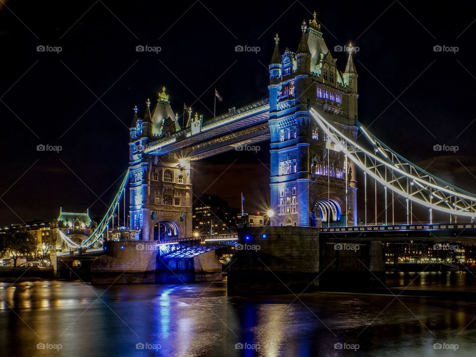 London tower bridge illuminated at night. River Thames in the foreground
