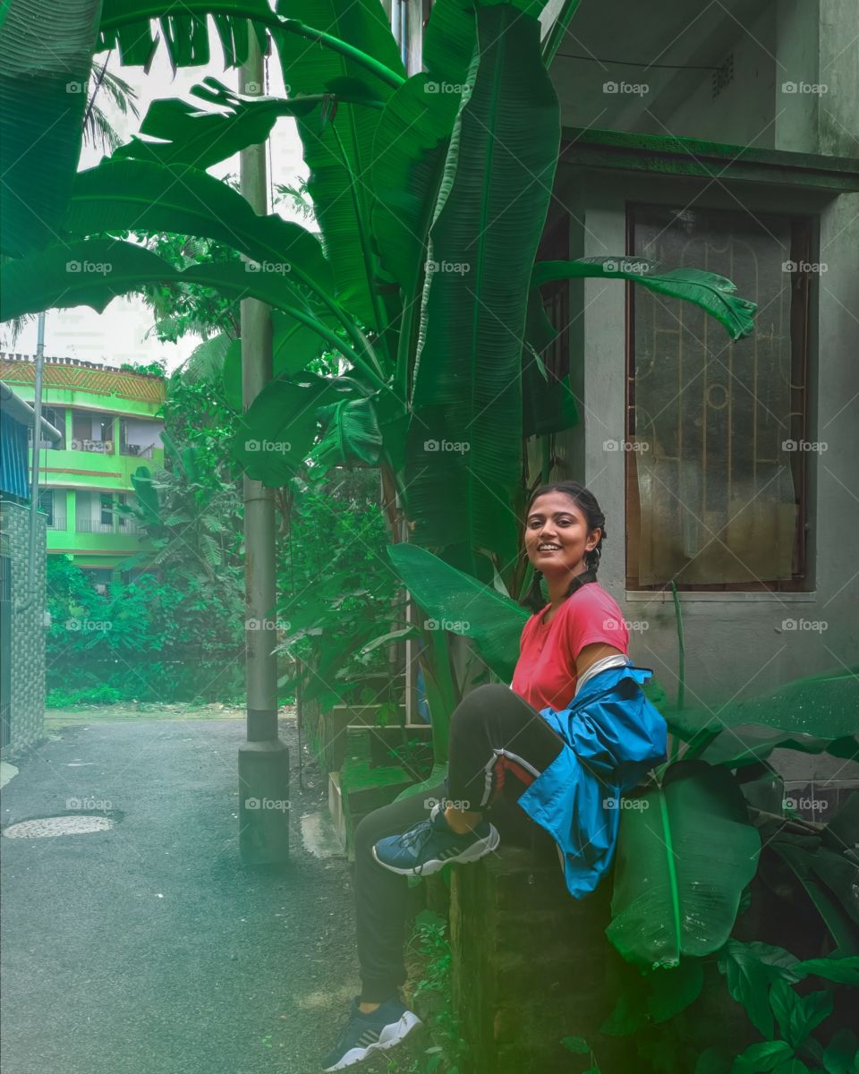 A girl is sitting under a banana tree happy and enjoying mother nature.