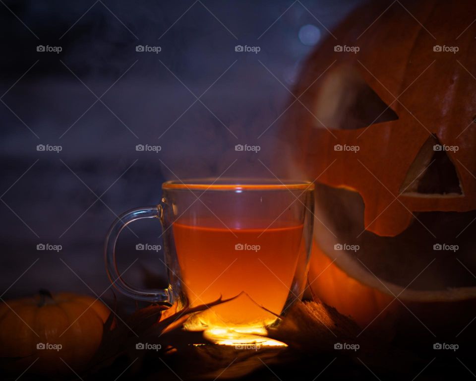 Hot cup of glowing cider in a spooky Fall setting with pumpkins