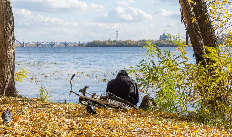 A men from behind with his bicycle on a river bank 