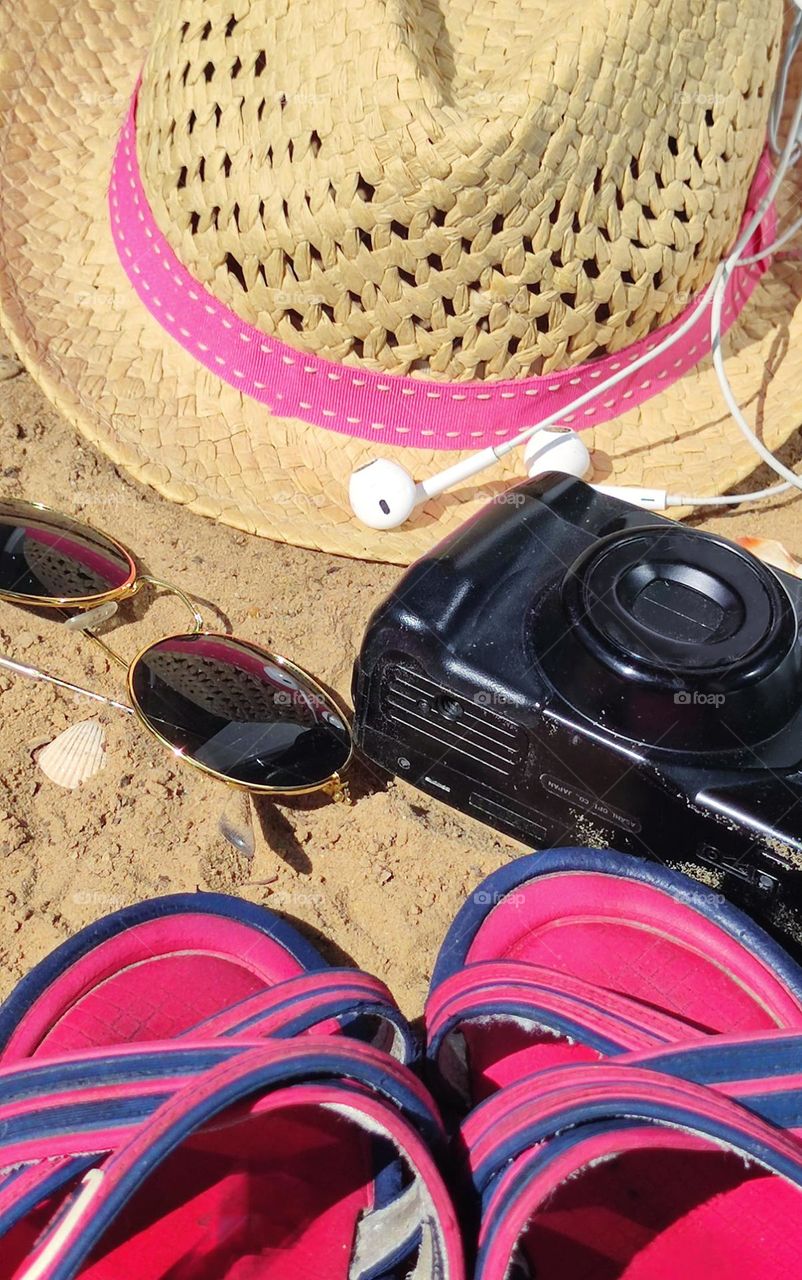 Essentials lie on the yellow sand: a straw hat, sunglasses, a camera, headphones and flip flops