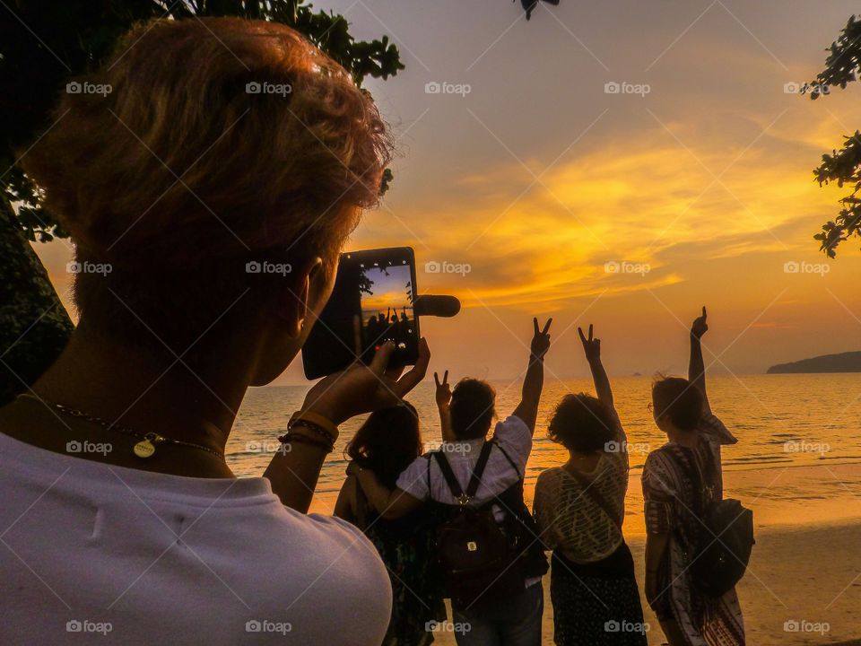 Taking a photo of a person taking a photo of friends at sunset