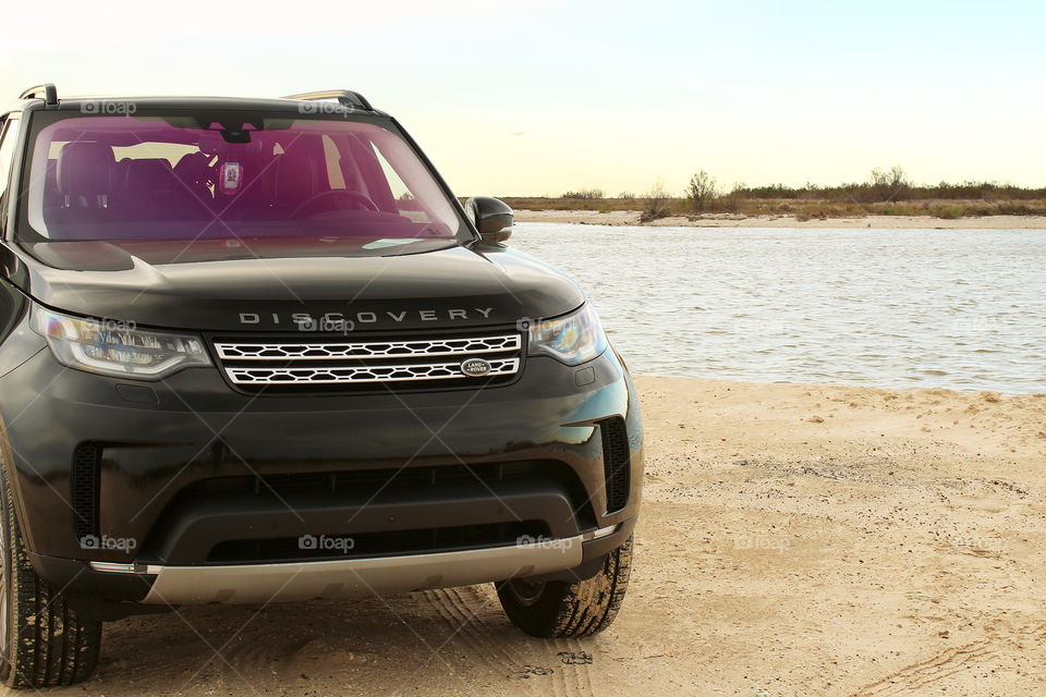 Black 2017 land rover discovery hse partial view on beach sand at sunset with ocean bay. Jetty park, matagorda, texas