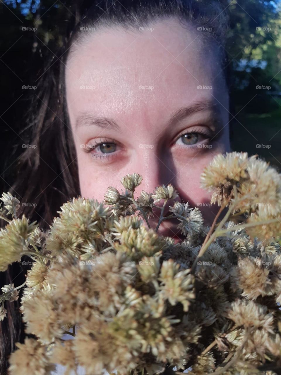 Mulher de olhos verdes com flores na frente do rosto.