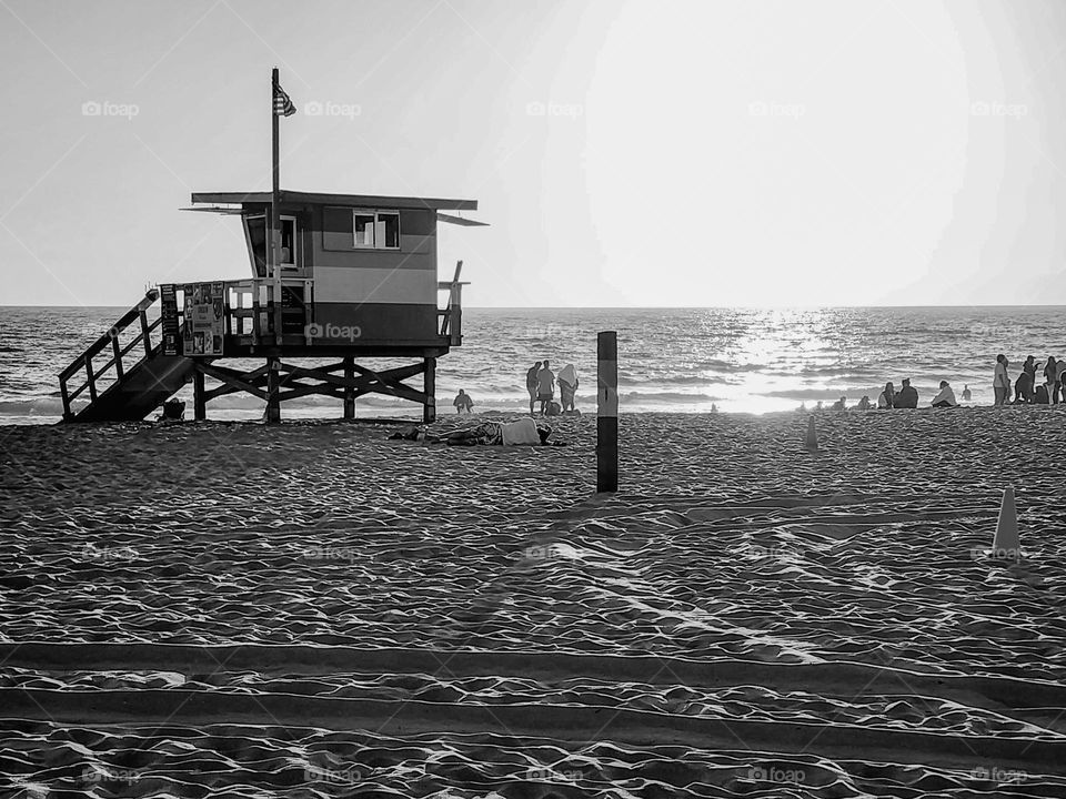 Sun sets on a California beach and a lifeguard watches over people from the stand