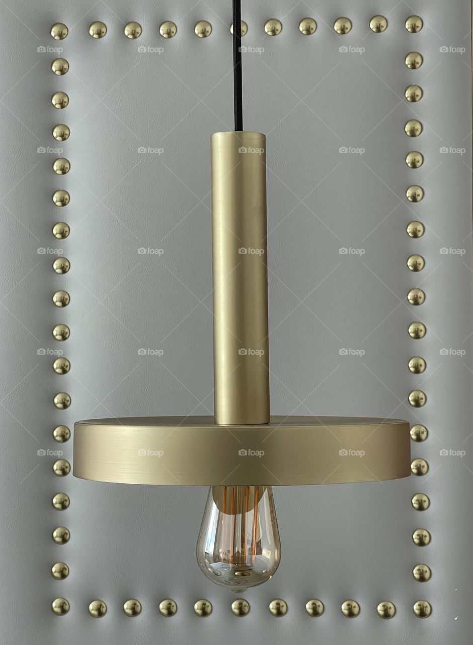 Modern golden metal lamp with light bulb against grey background decorated with metallic studs 