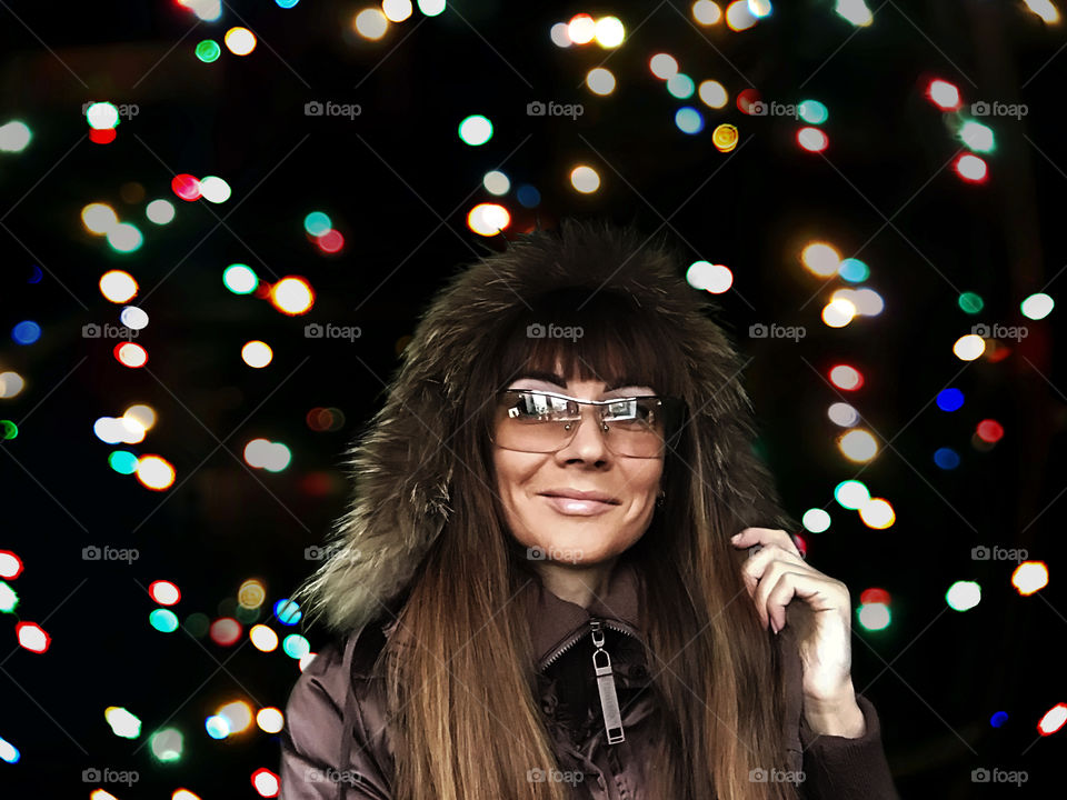 Portrait of a young smiling woman in winter clothes in front of colorful festive night lights