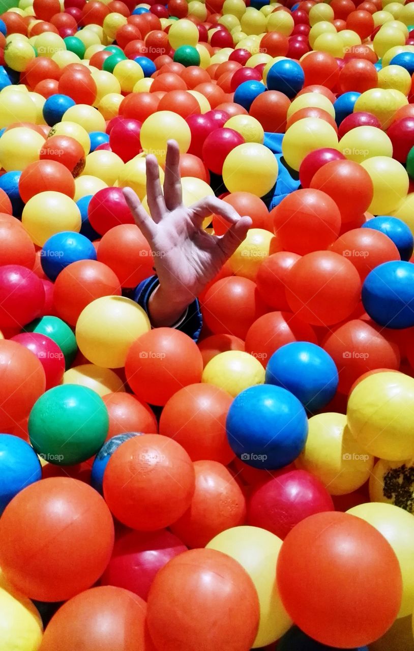 ball pond full of coloured balls and one hand saying ok