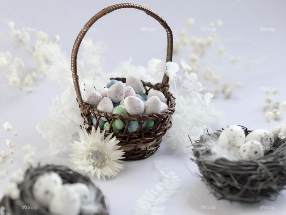 Chocolate eggs in a basket surrounded by white dried flowers and birds nests. 