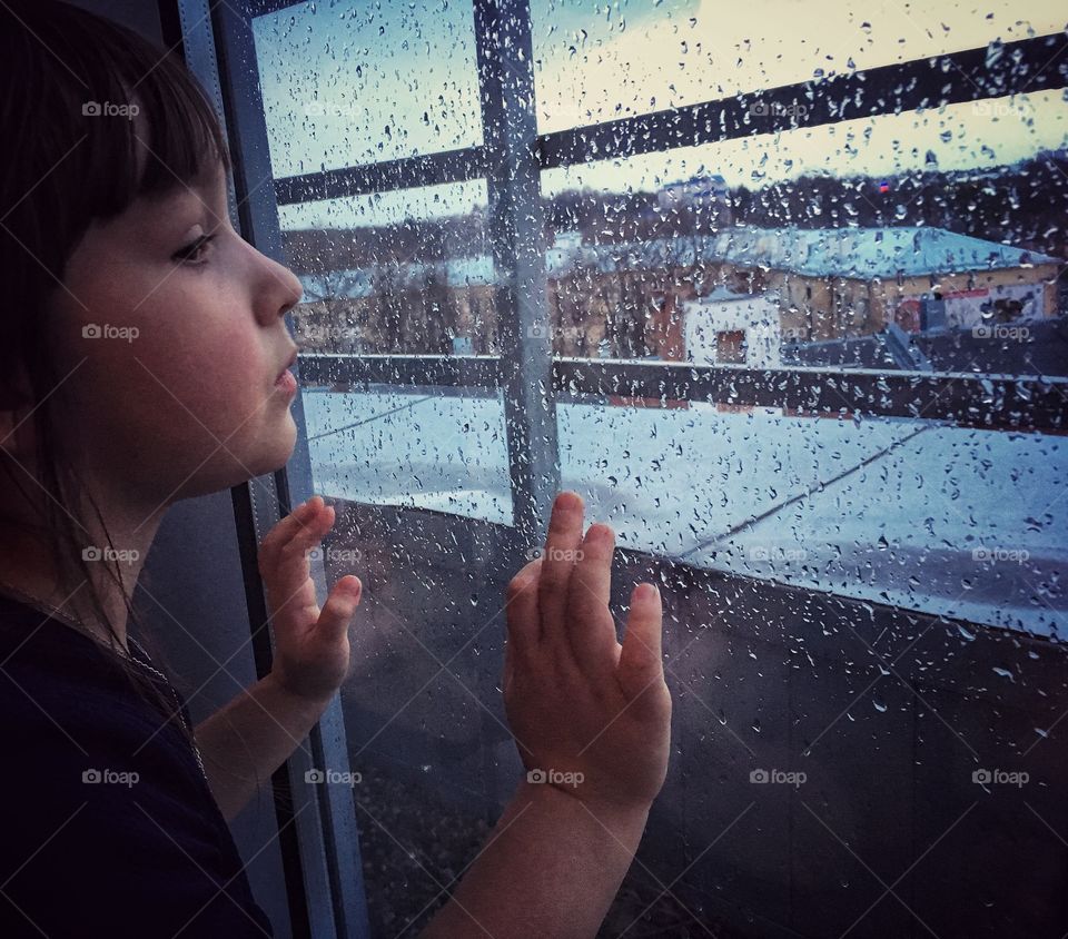 Girl looking through the window on rainy city 