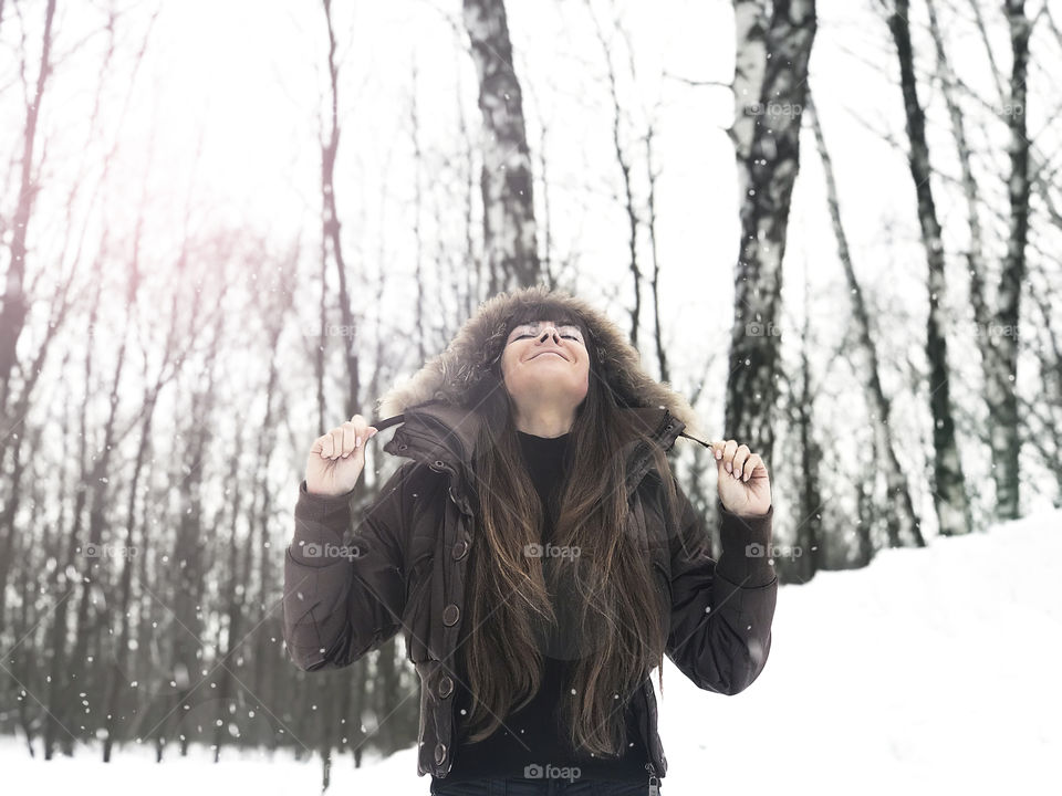 Young woman with long hair happy under the falling snow in winter forest 