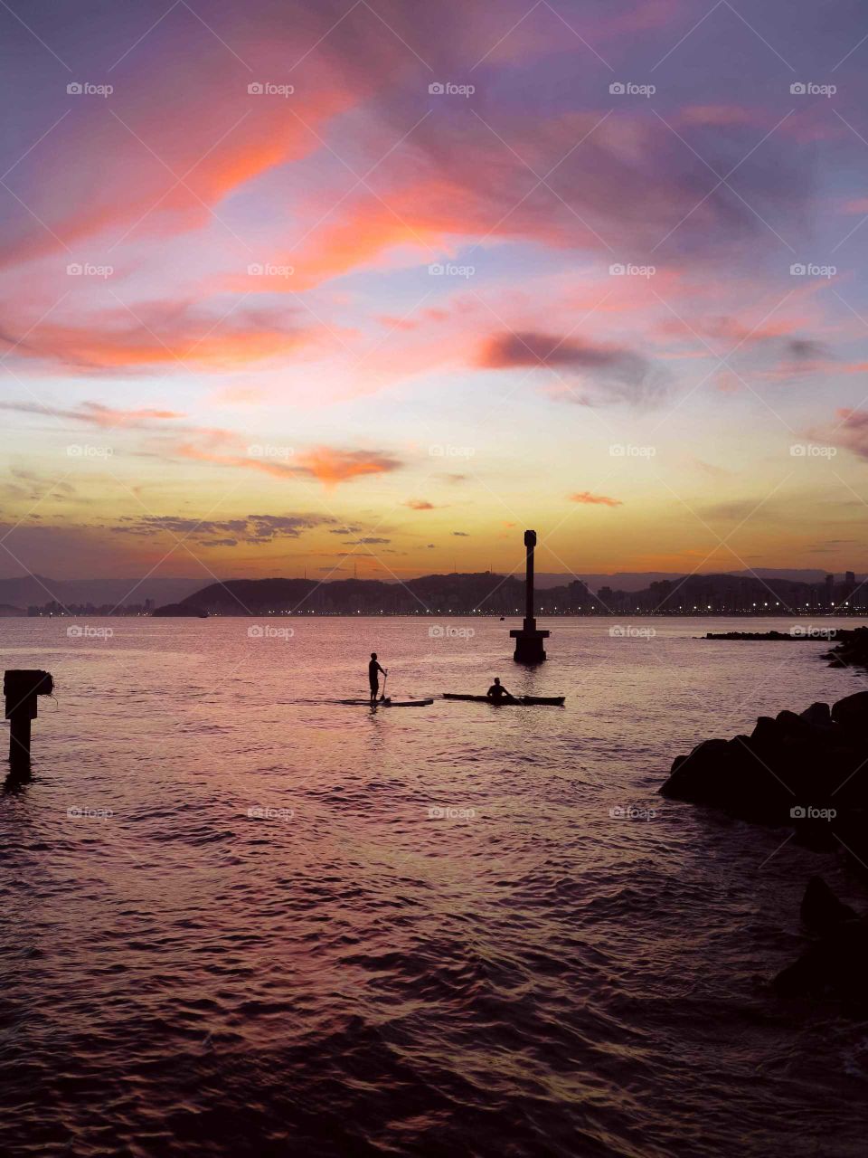 Sailing/surfing/kayaking men at Santo's Bay, Brazil. Beautiful Sunset,  with purple and orange tones.