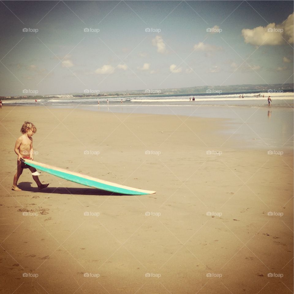 Surfer little boy . Walking down the beach of Bali where the surfer spirit is so alive , little kid following big waves 