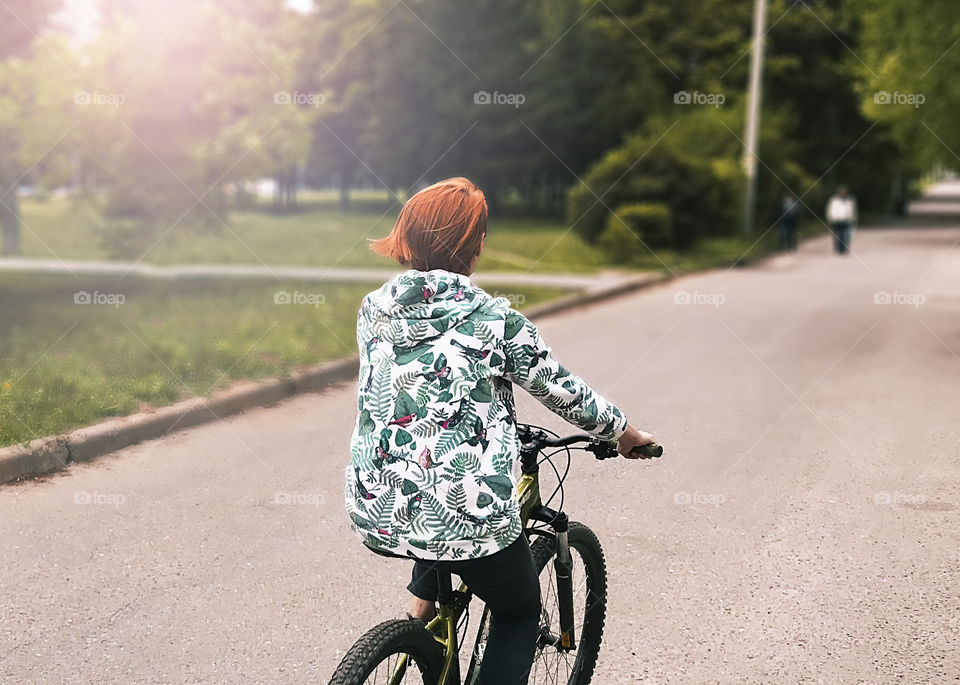 Young red haired woman riding a bicycle by the street 