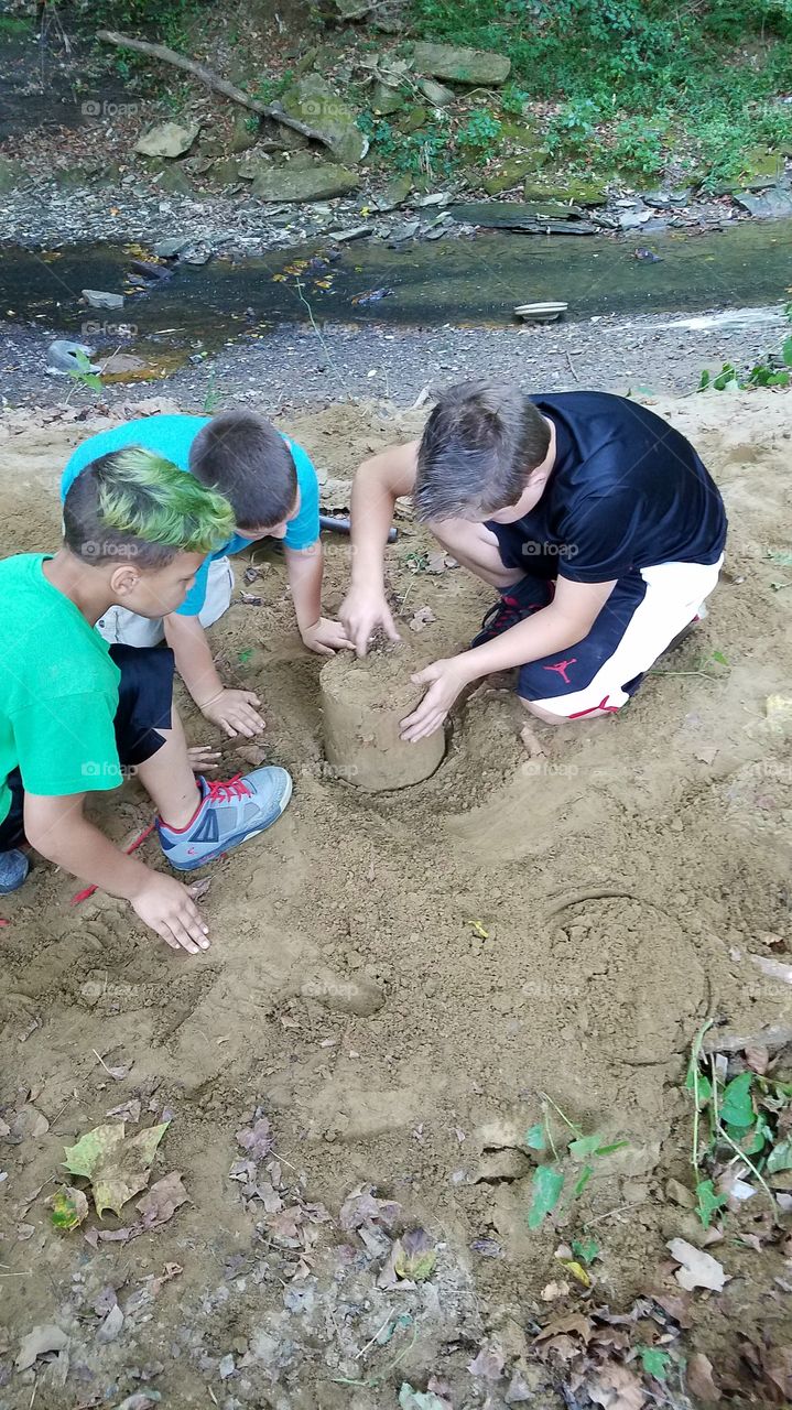 Children making fort with sand near stream