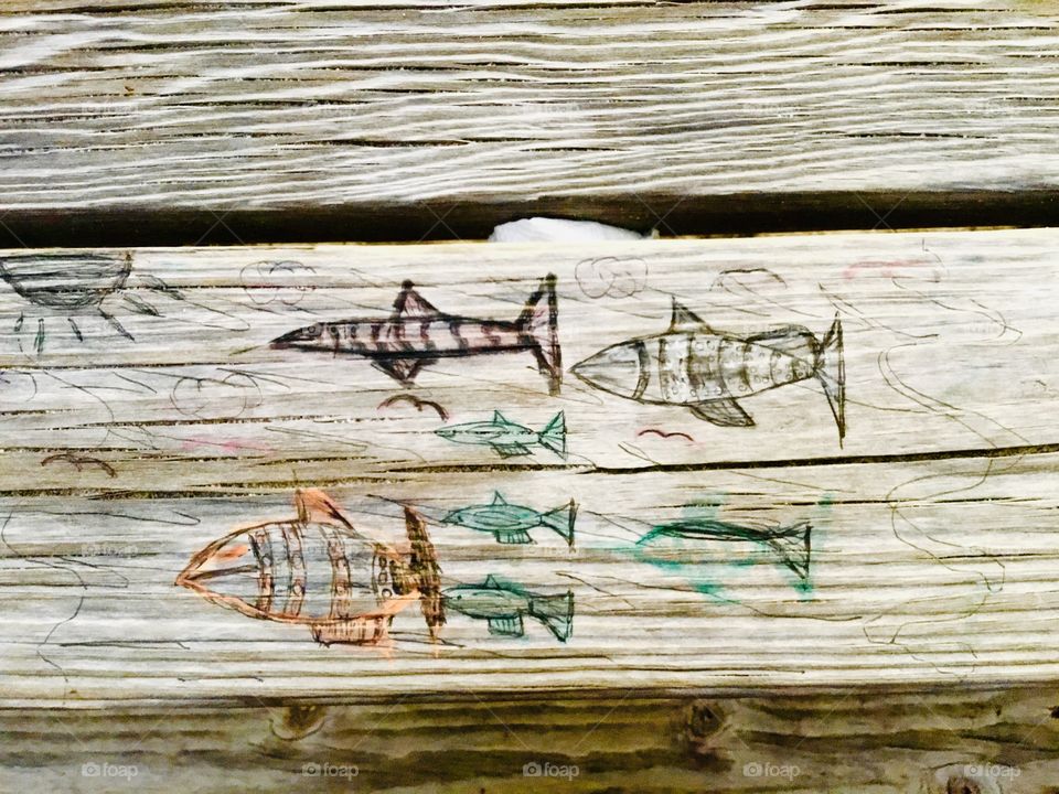 
Someone carved these designs in a wooden picnic table. Carving is the act of fashioning or producing by cutting into or shaping solid material, as wood. a carved design or figure.