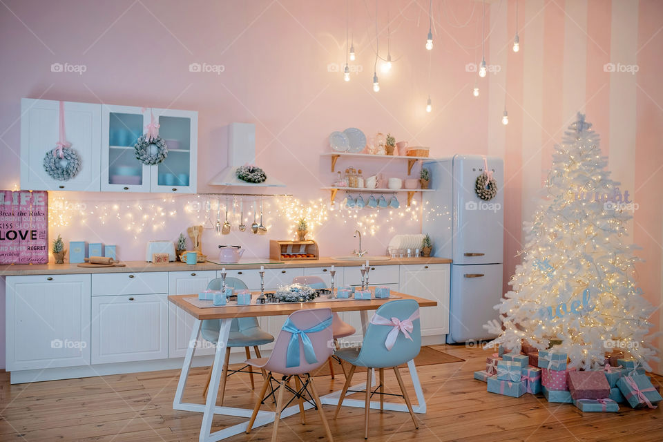 Festive winter cozy kitchen interior with garlands, decorations and gifts.  Christmas dinner at the decorated table.