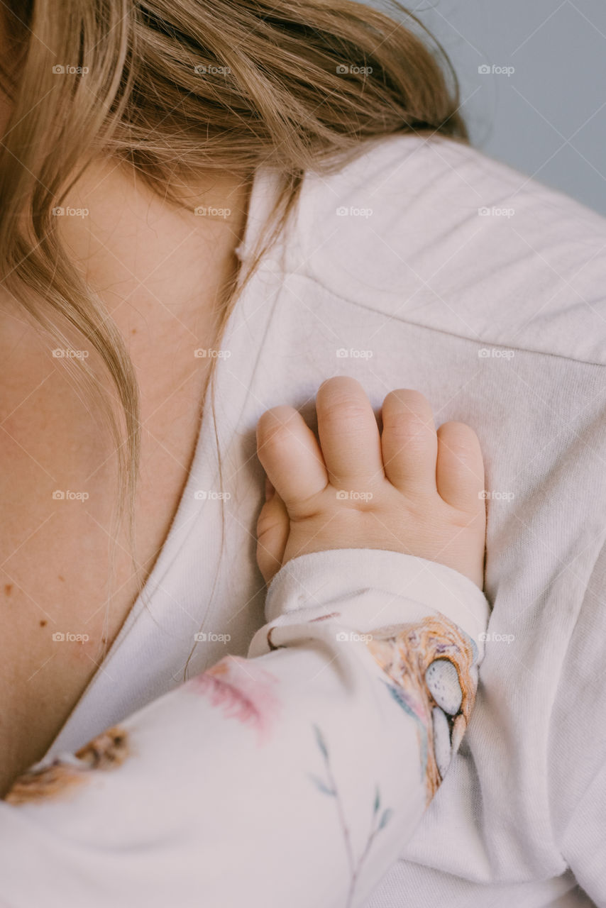 Toddler’s hand resting on her mother. Breastfeeding. Details of motherhood.