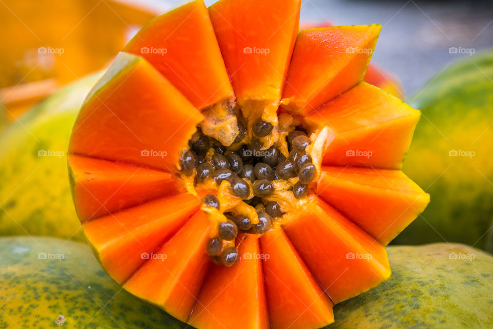 Artfully cut bright orange papaya sitting on other papayas