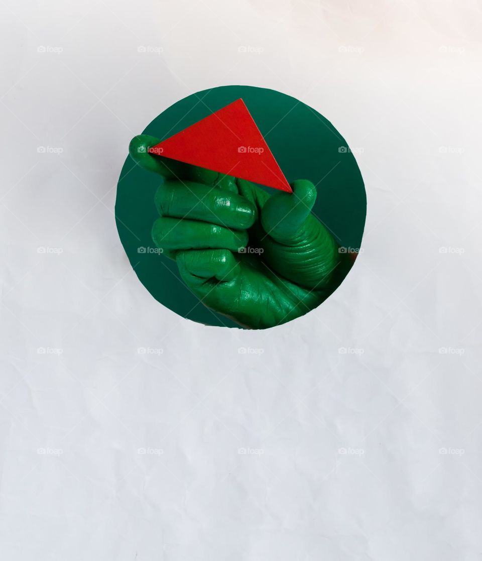 Green painted hand holding red triangle.