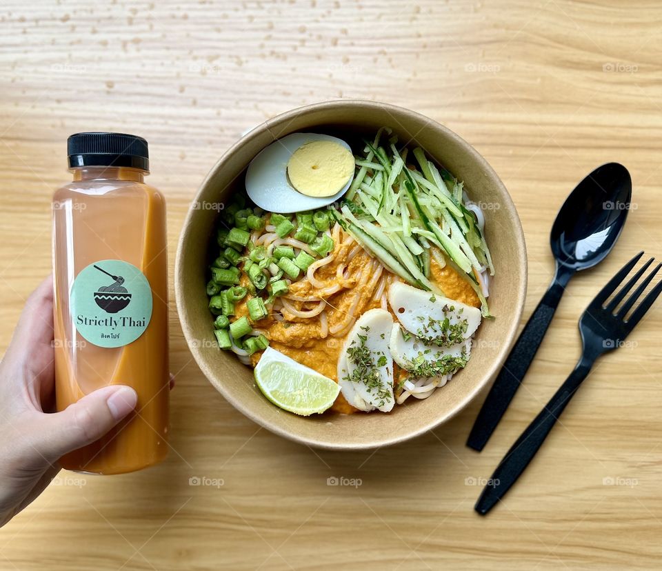 Khanom jeen namya thailand dry laksa fish with fish curry, boiled egg, fresh greens and fishcake slices and Thai milk tea 