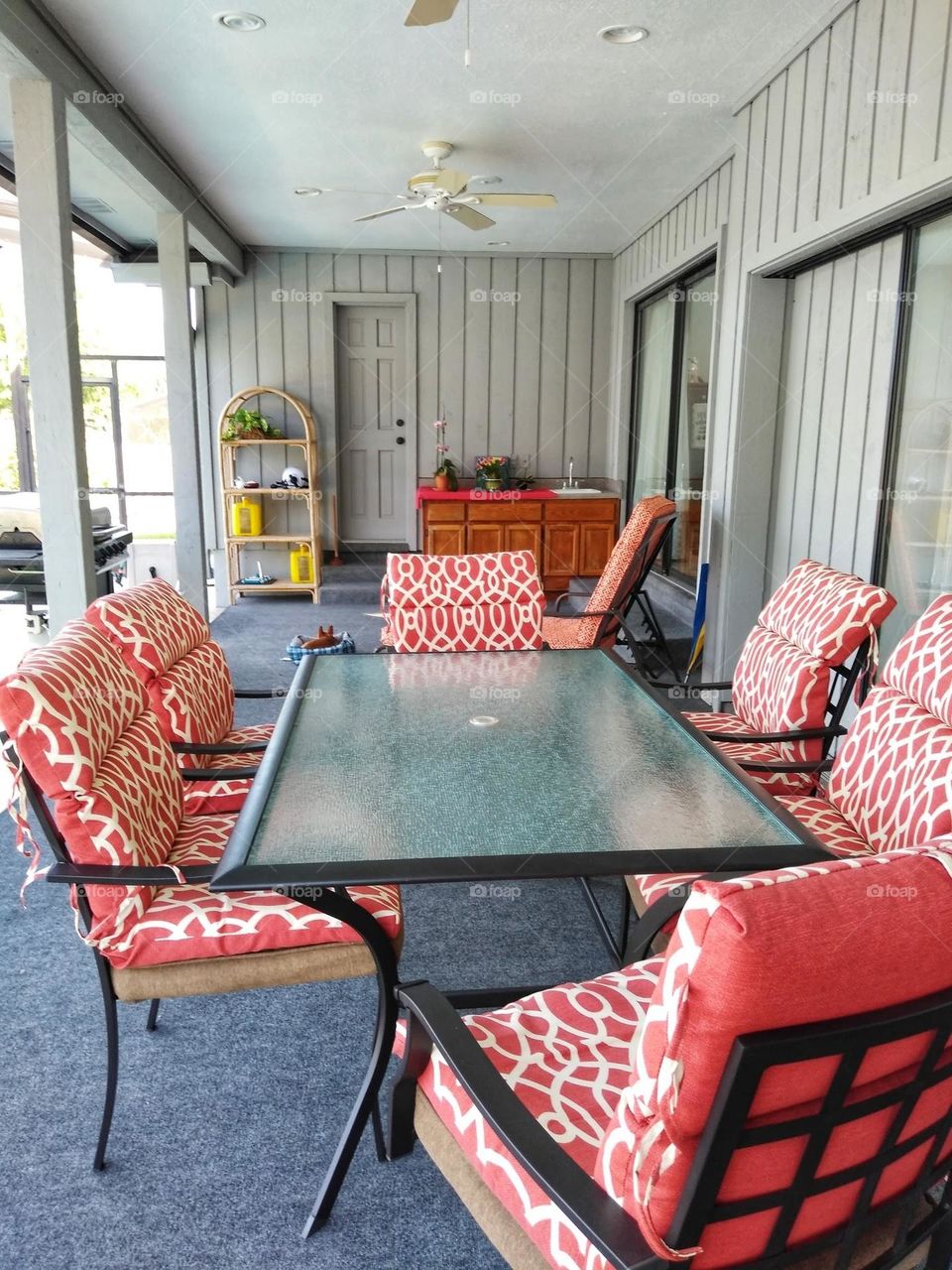 A beautiful backyard patio with a dining table and orangish red chairs around it. The patio is covered and there is also a pool off to the left.